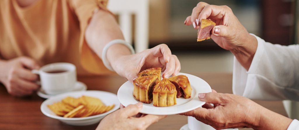 Mooncakes served on a plate with hands reaching for pieces of cake
