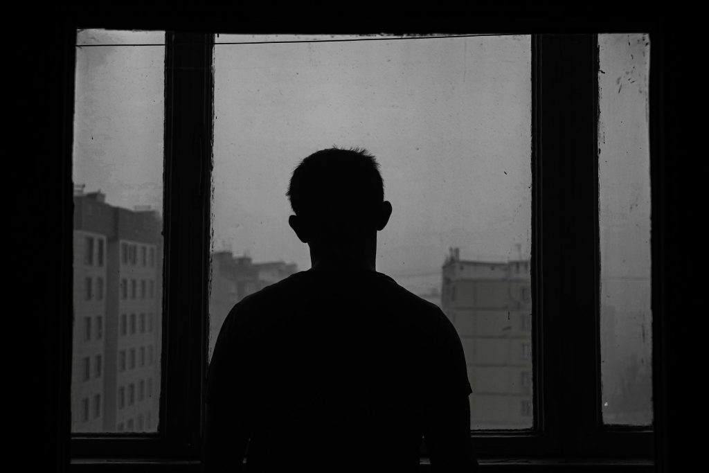 dark photo with a man looking out a window, the photo has vibes of depression
