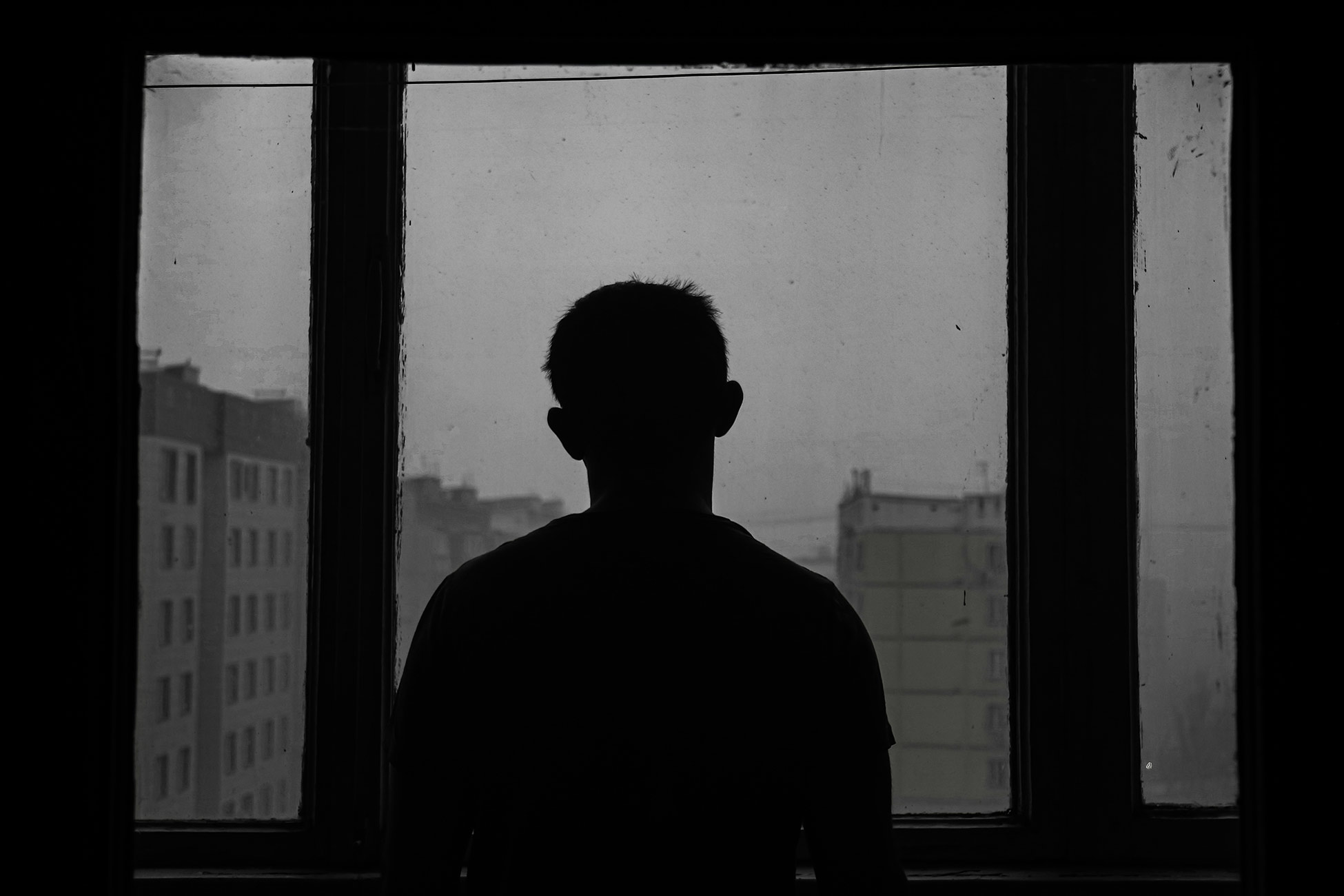 dark photo with a man looking out a window, the photo has vibes of depression